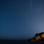 Meteoros a riscar um céu estrelado sobre uma falésia rochosa