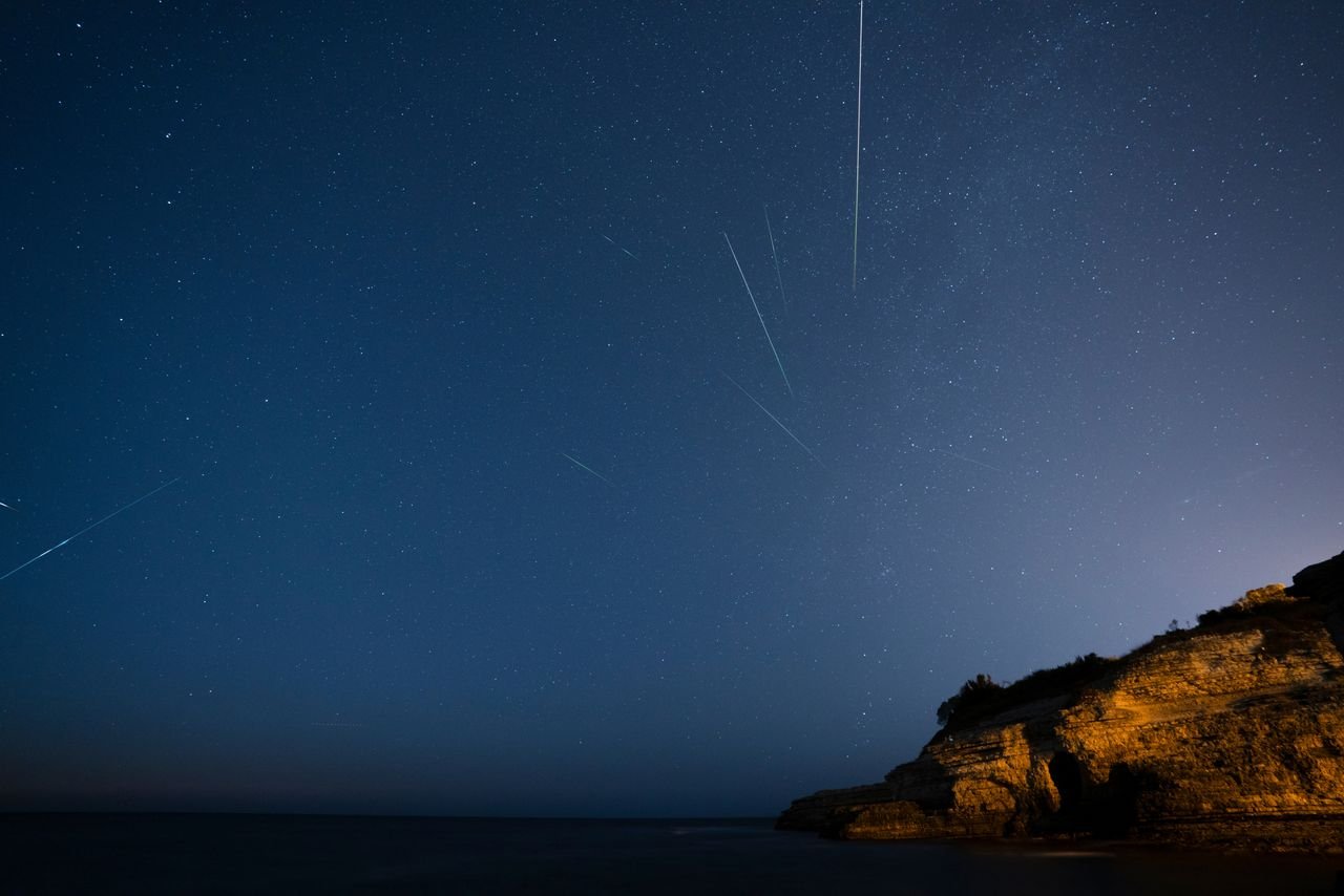 Meteoros a riscar um céu estrelado sobre uma falésia rochosa