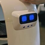 Robô de serviço branco com ecrã de olhos azuis a levar pratos