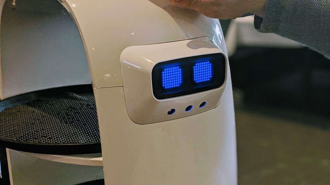 Robô de serviço branco com ecrã de olhos azuis a levar pratos